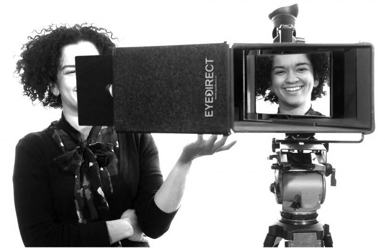 Woman smiling through camera viewfinder setup.